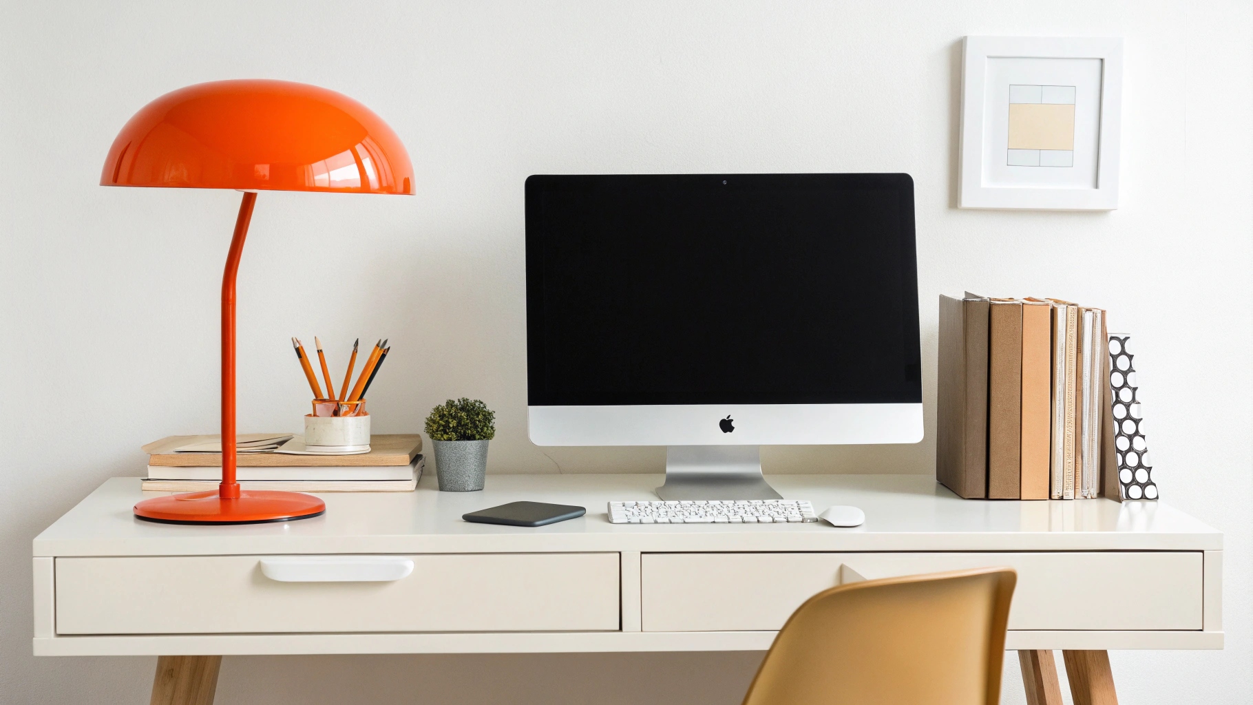 A glossy orange mushroom lamp adds a pop of retro color and energy to a minimalist white home office desk with a computer.