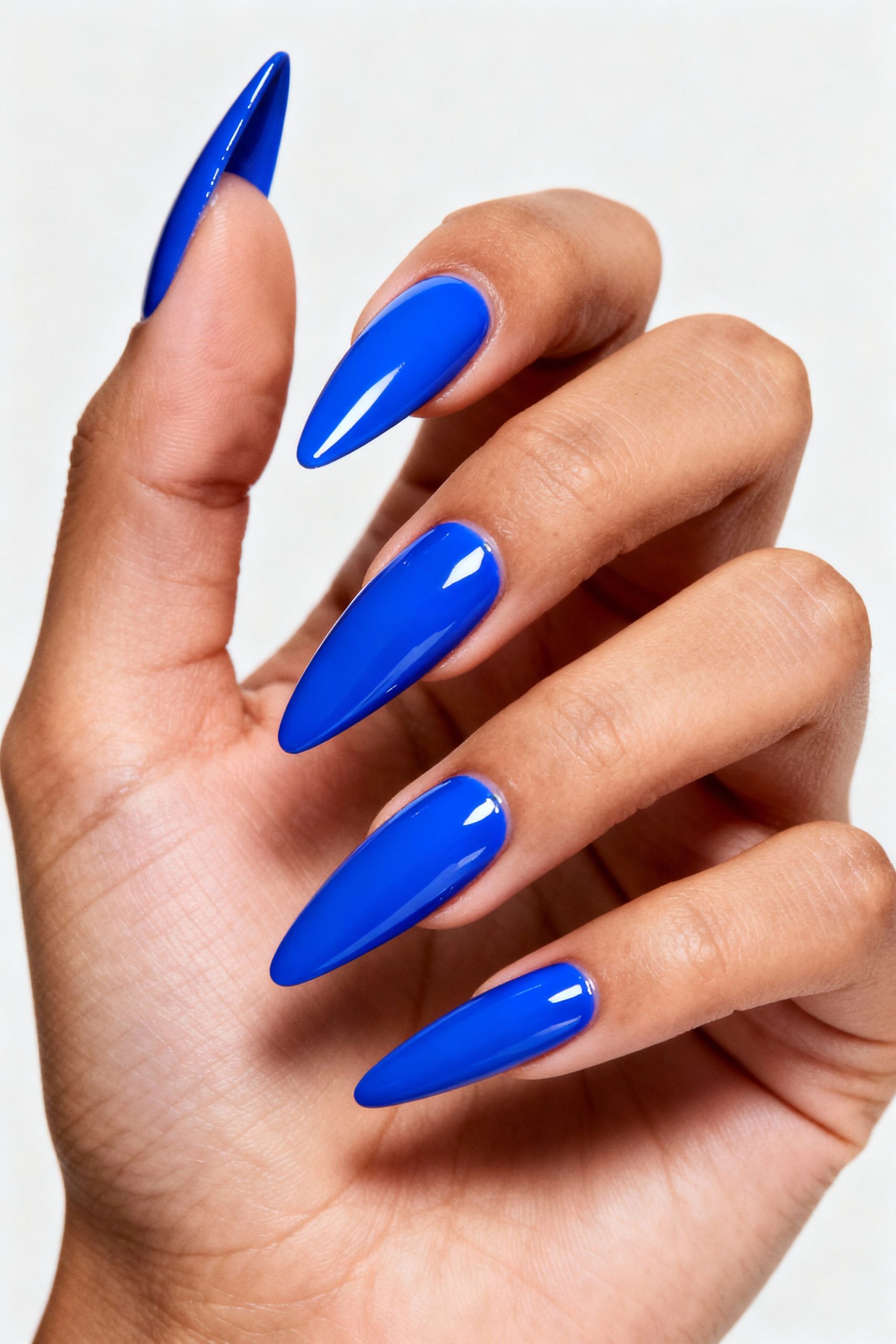 A hand displaying long, glossy stiletto nails painted in a vibrant, solid cobalt blue polish against a white background.