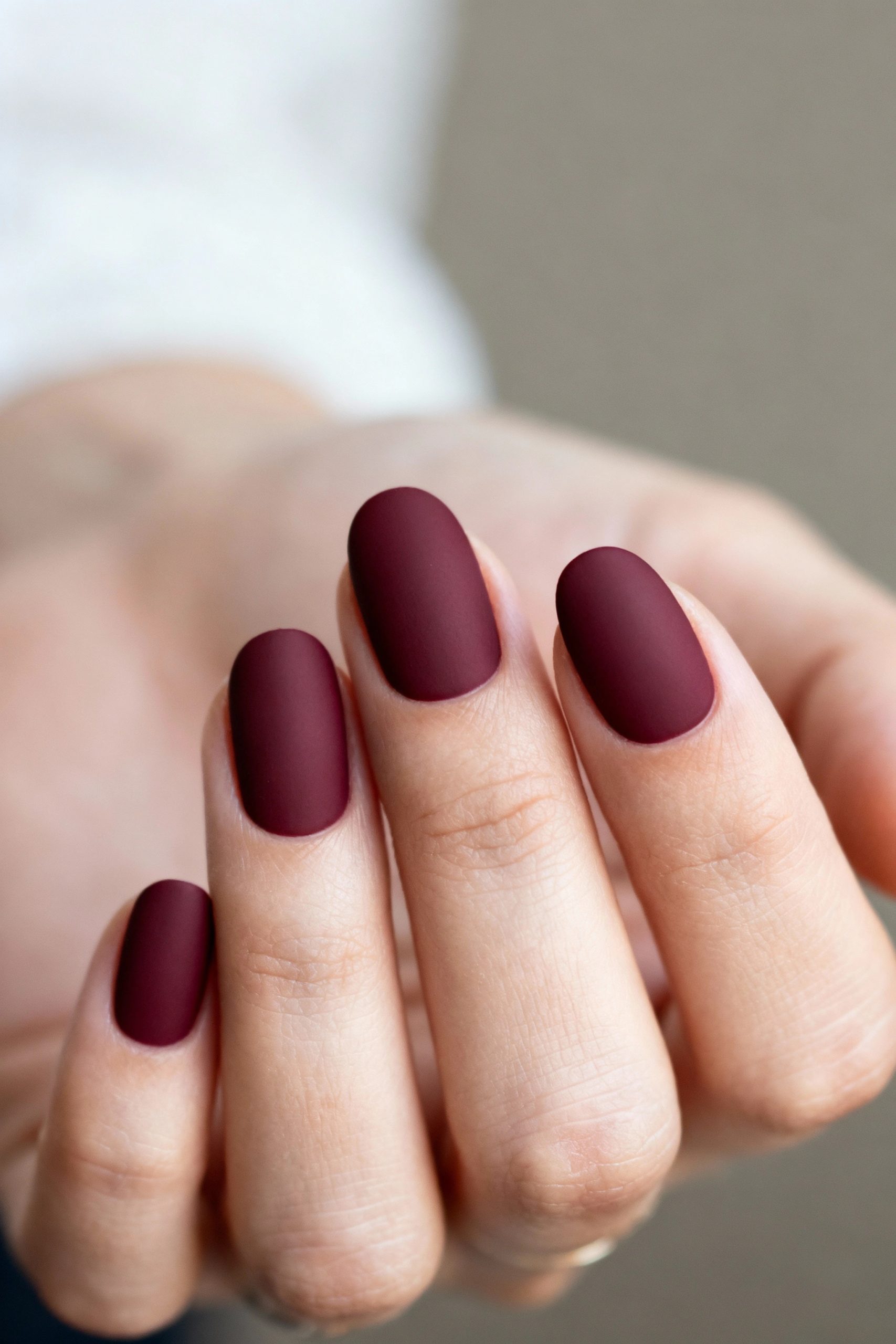 A close-up of fingers with medium-length oval nails painted in a deep, solid burgundy color with a velvety matte finish.