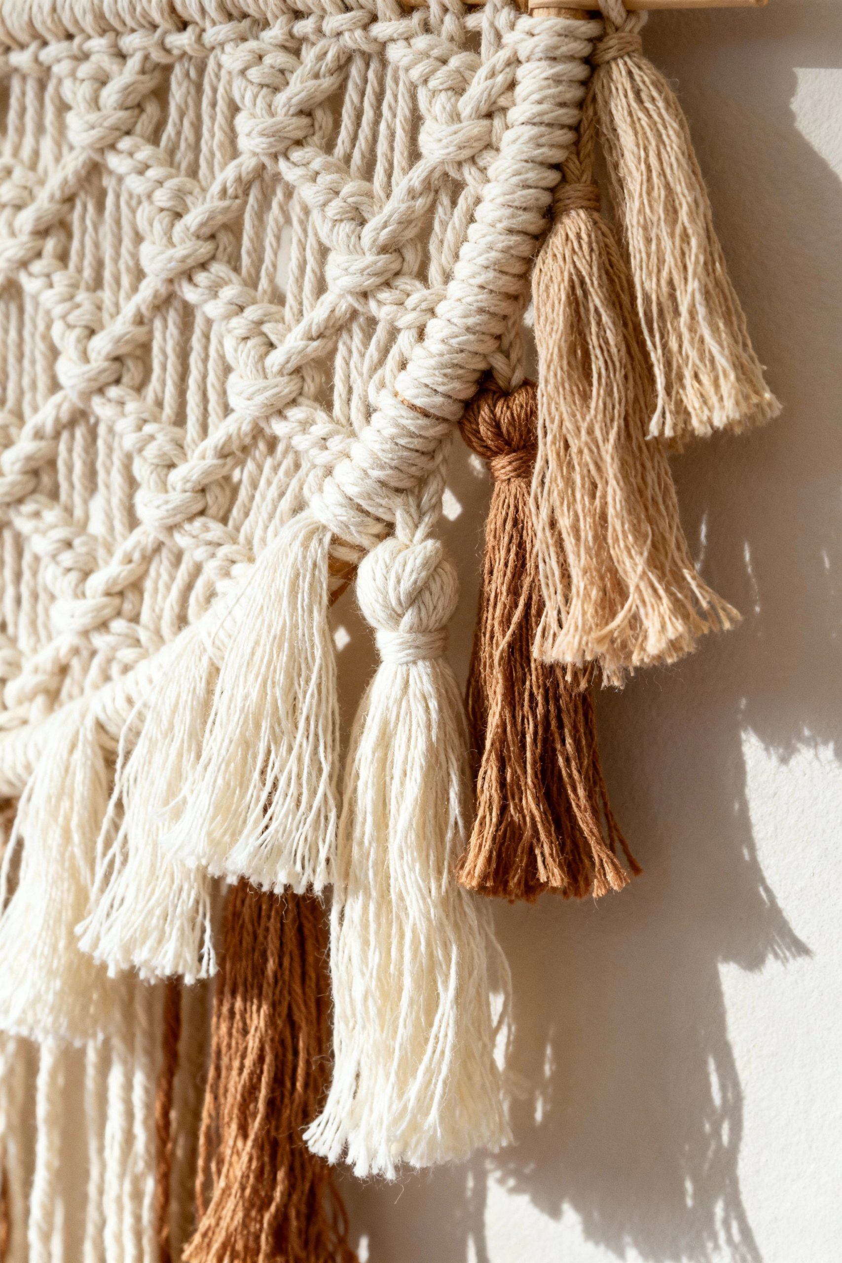A sunlit close-up of multi-toned macrame tassels in white, beige, and brown, showcasing texture and color variation.