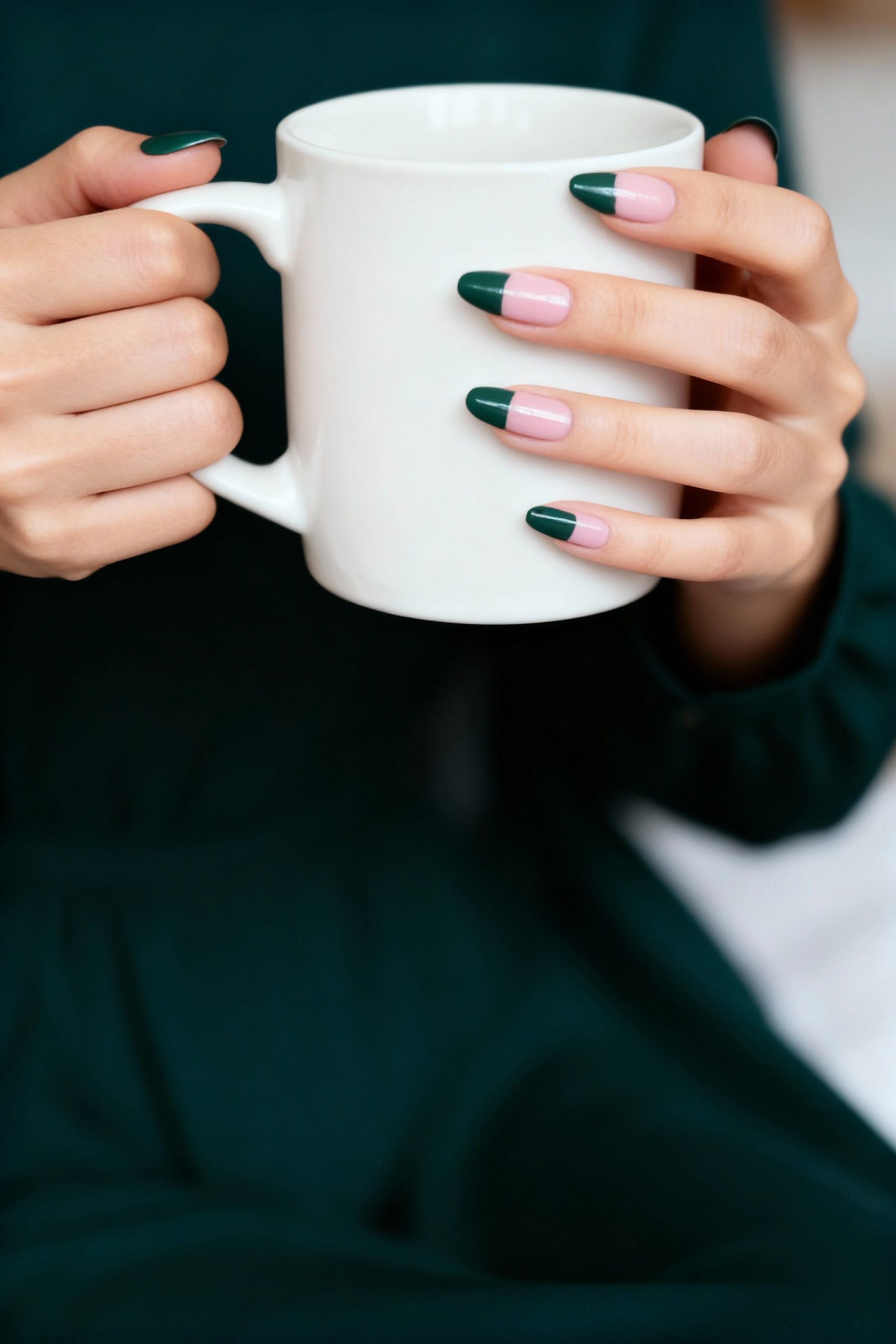 Close-up of a woman's hands holding a white mug, showcasing a modern French manicure with deep forest green tips.