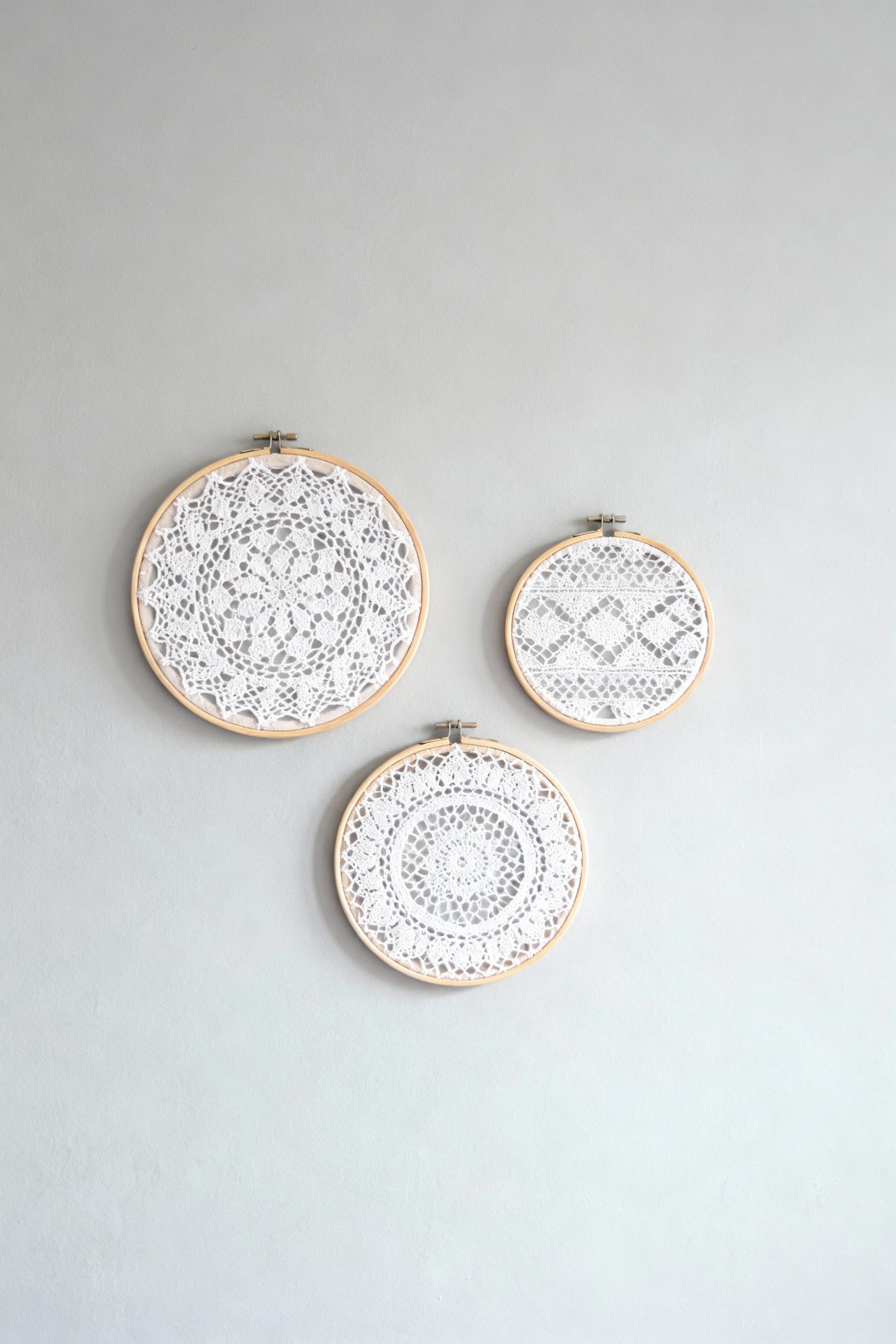 Three embroidery hoops of different sizes displaying different white lace patterns, arranged as beautiful, simple wall art on a light gray wall.
