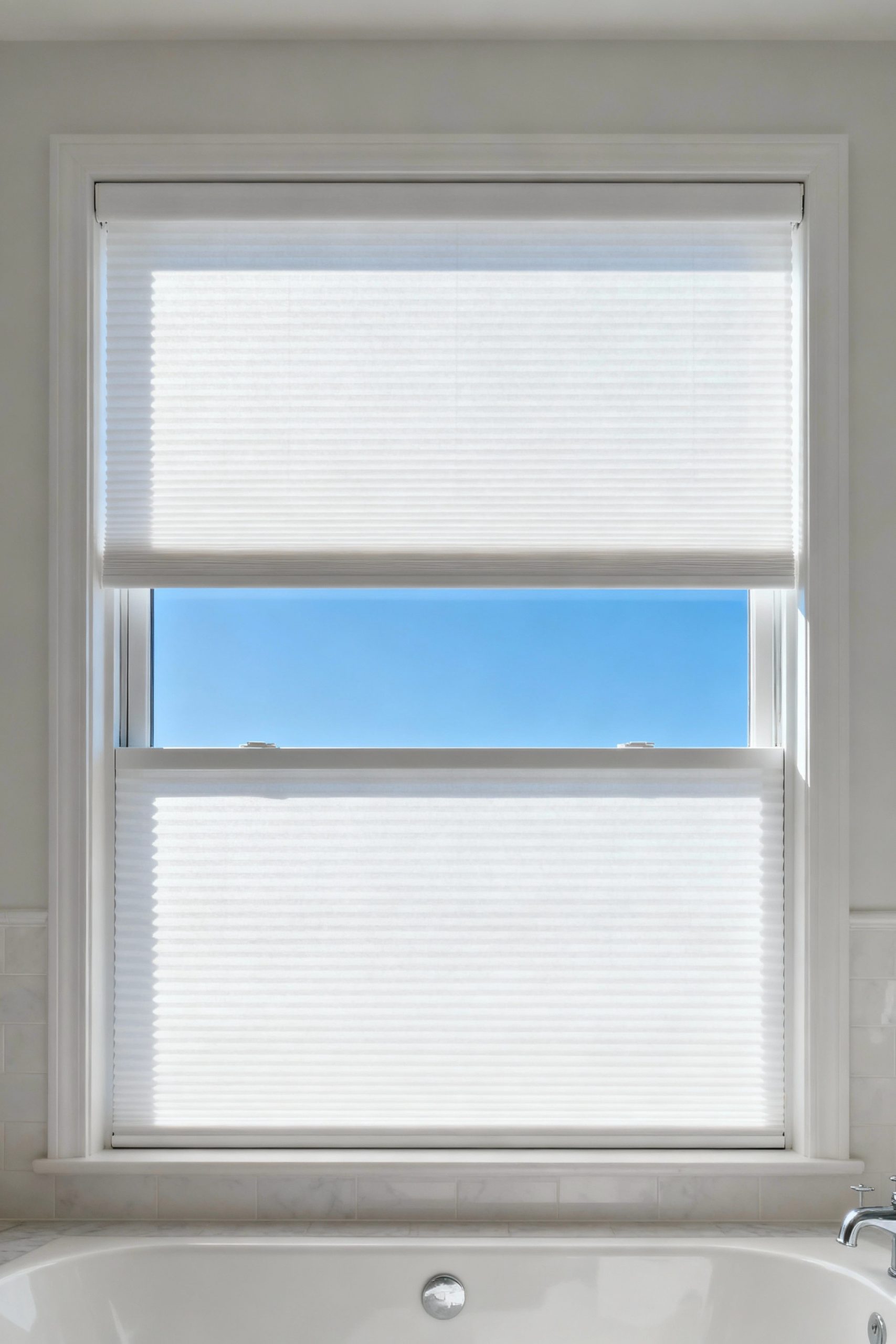 A white top-down, bottom-up cellular shade on a bathroom window is lowered from the top to let in light and show the sky while maintaining privacy below.