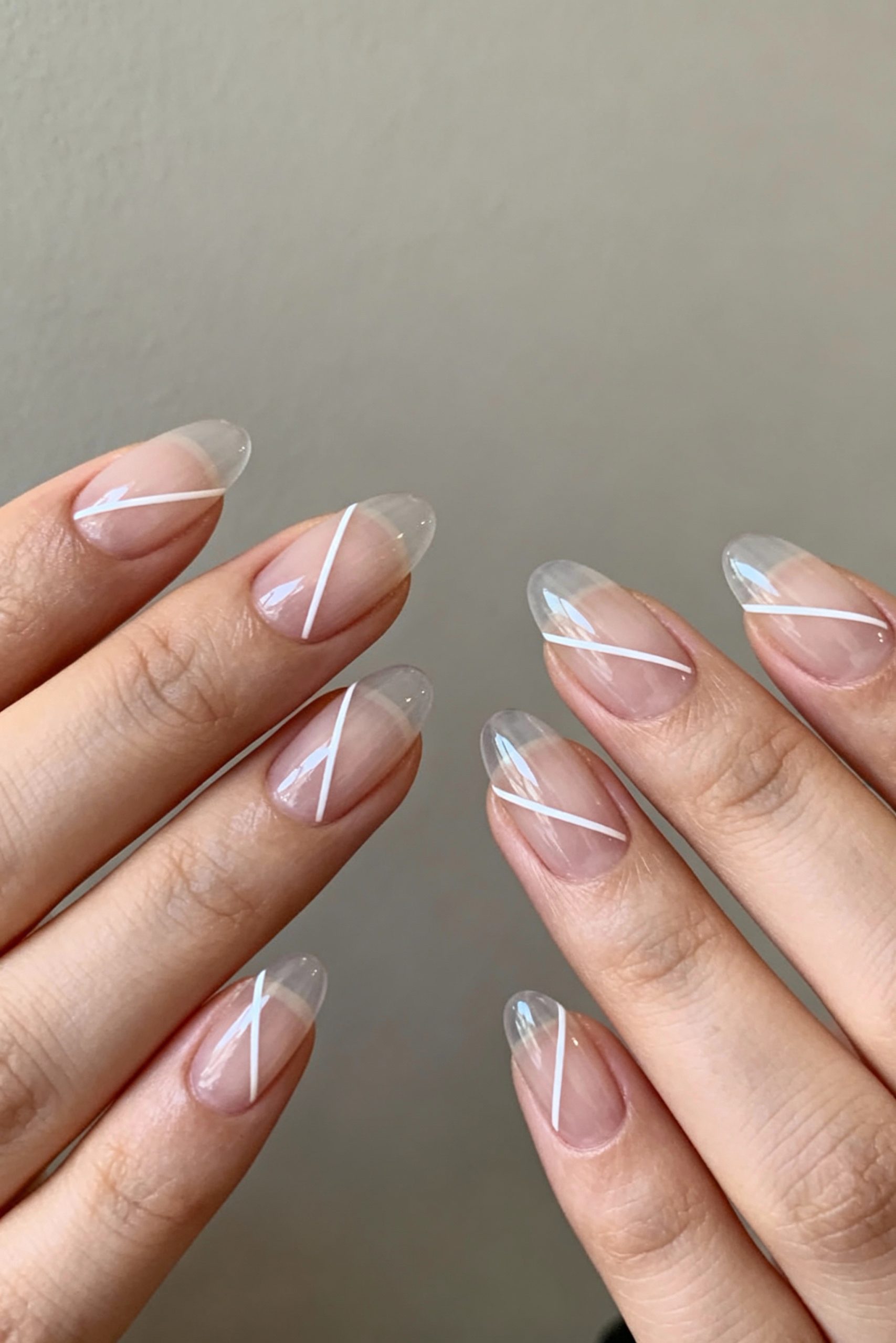 Close-up of two hands showing a geometric nail art design with crisp white lines on a clear, glossy almond-shaped nail base.