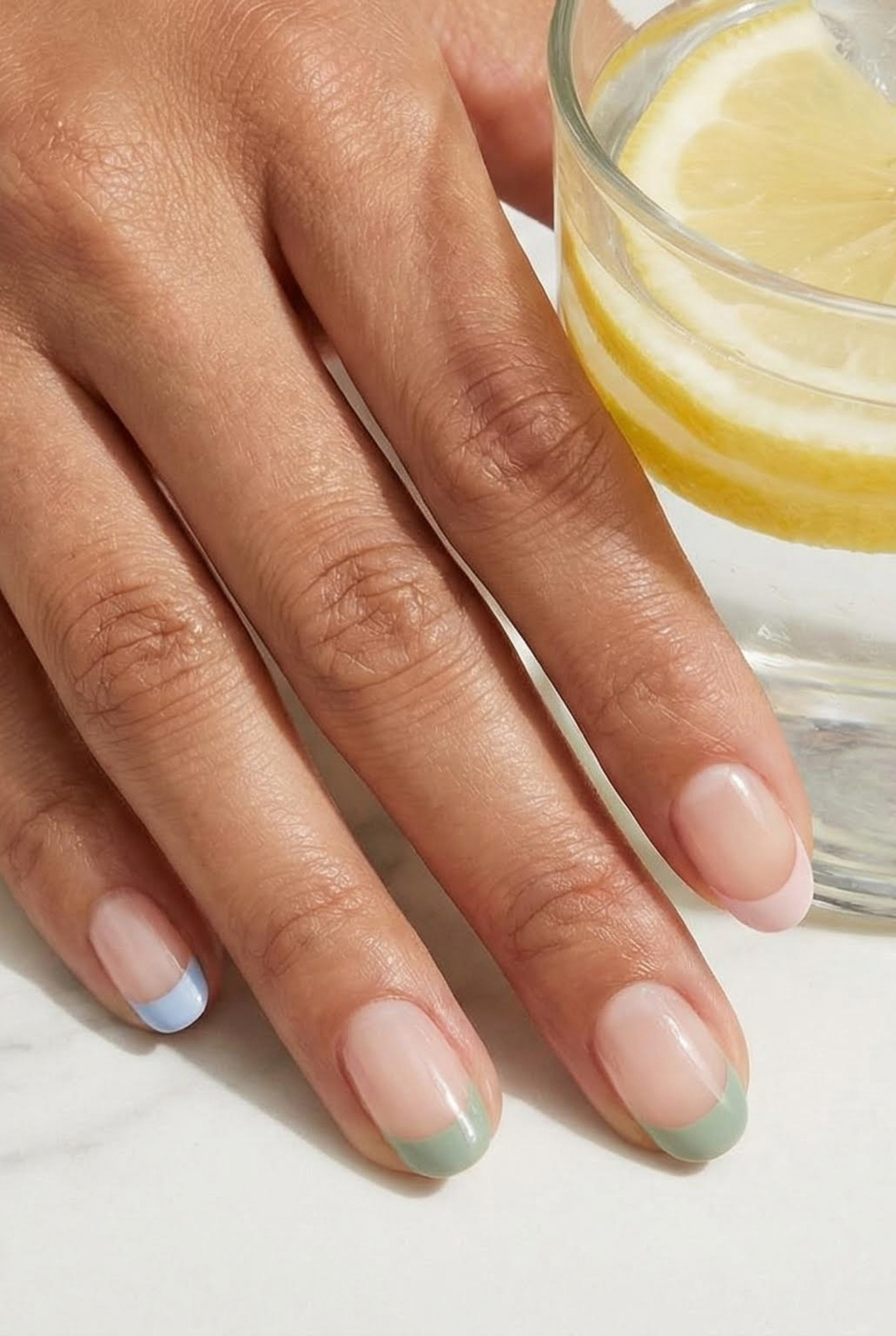 Minimalist Chic: The Ultimate Guide to the Modern Micro French Manicure 2 Hand holding a glass of lemon water, featuring micro french manicure with pastel blue, green, and pink tips.