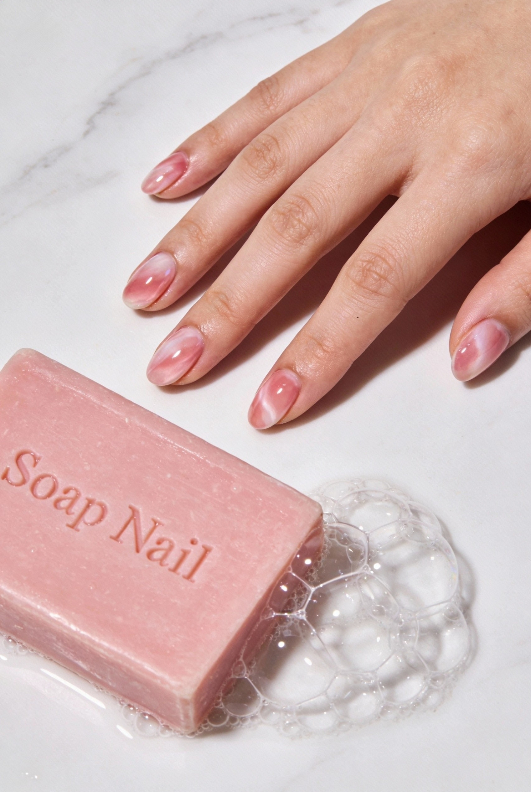 The "Soap Nail" Trend for an Ultra-Clean Aesthetic 2 Hand next to a pink bar of soap and bubbles, showing off milky rose colored nails.