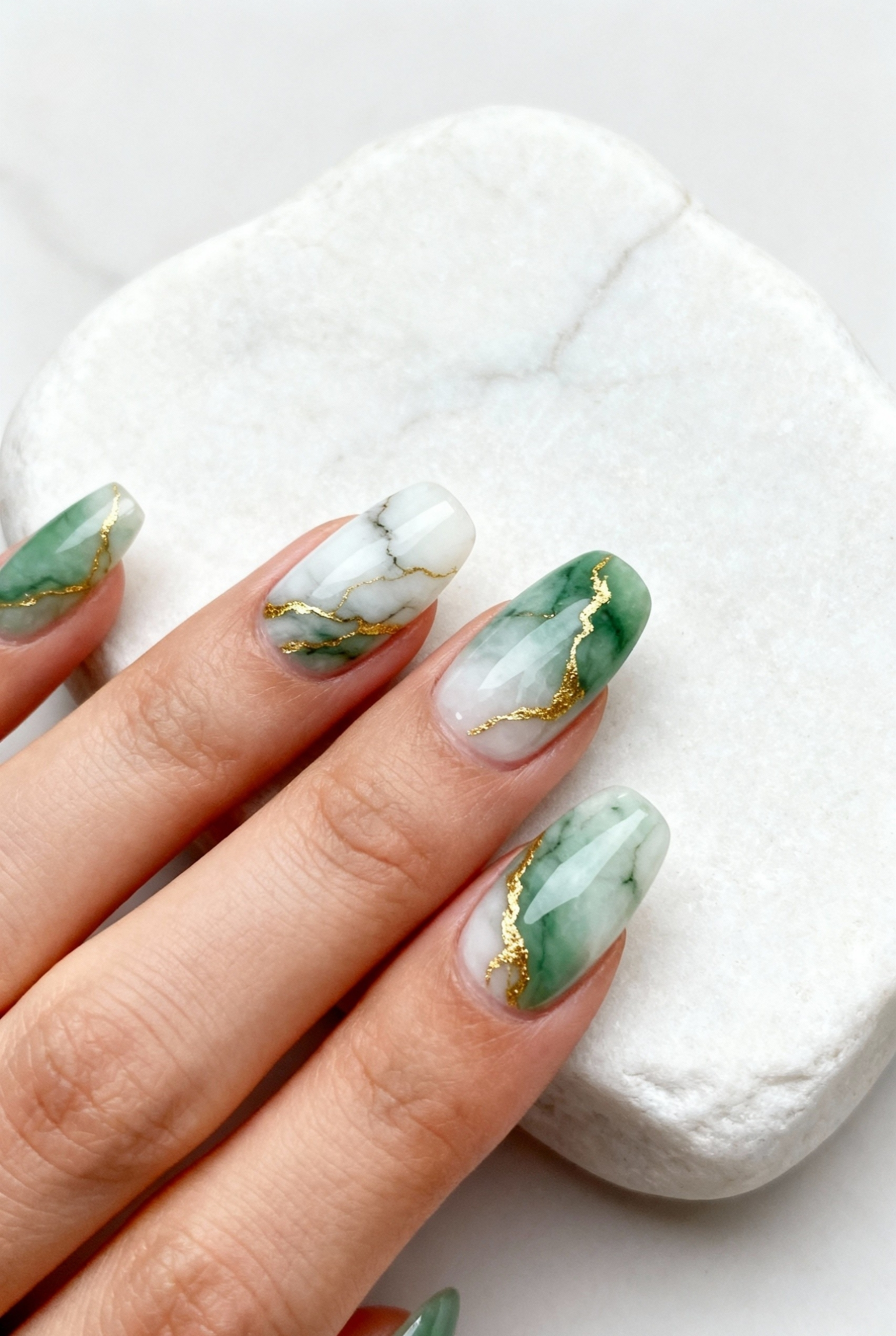 Almond shaped nails featuring a marble design with sage green, white, and gold veins resembling jade stone.
