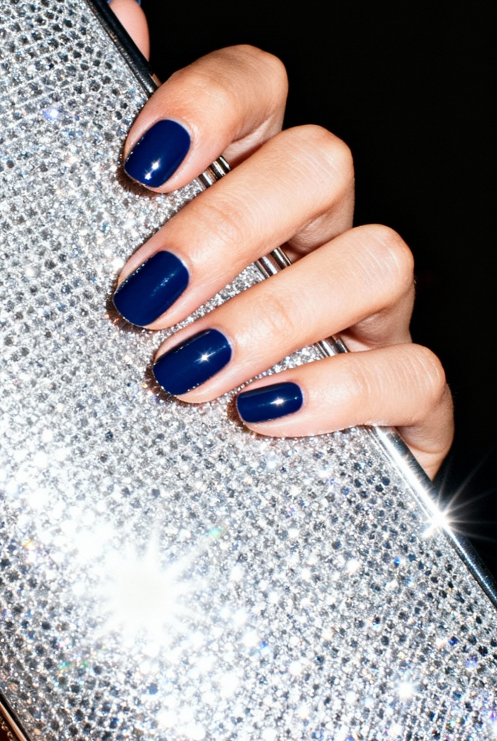 Sophisticated Depth: The Midnight Blue and Navy Nails Manicure 7 Woman's hand with glossy midnight blue nails holding a sparkling silver evening clutch bag with flash photography style.