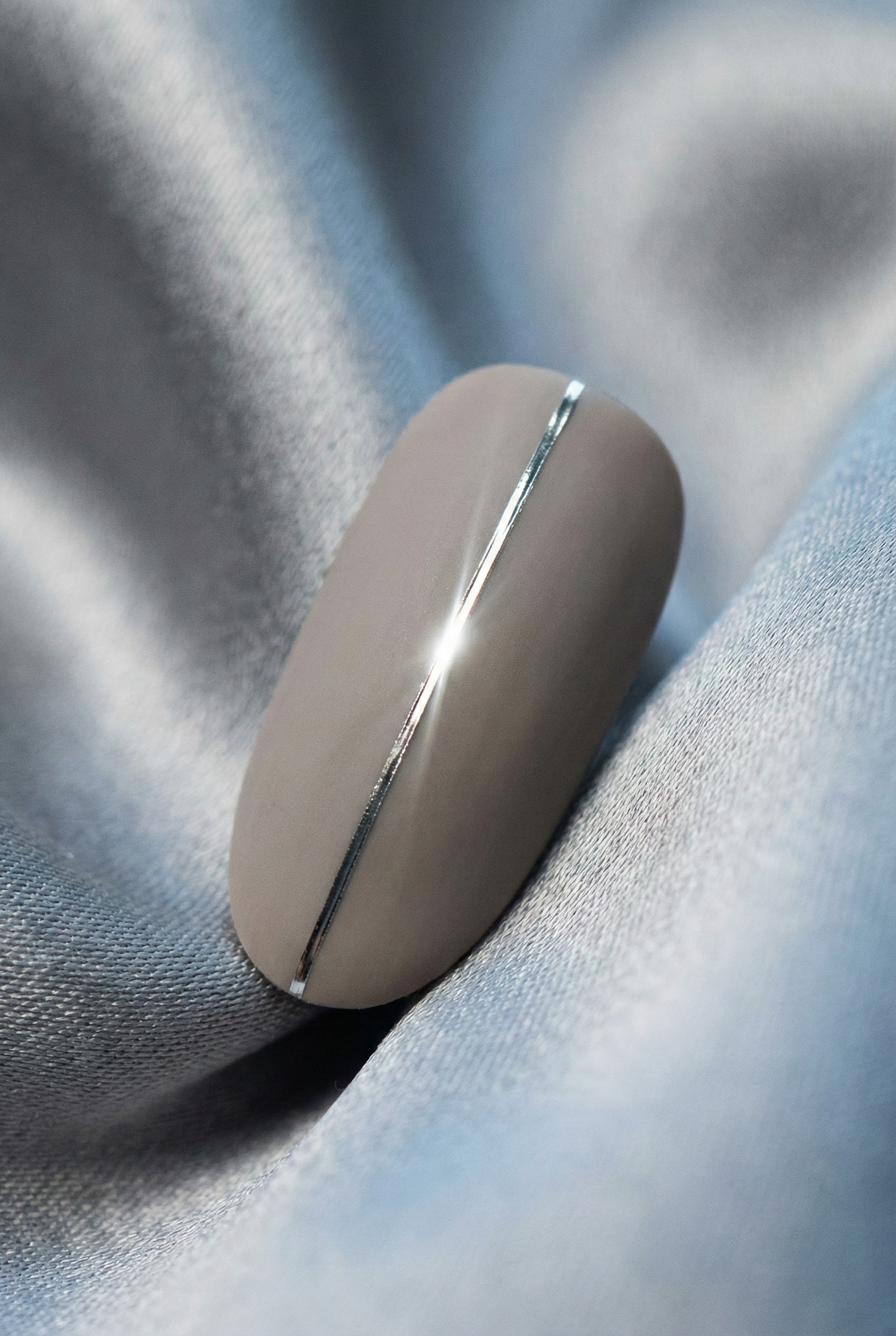 Macro photography of a greige nail featuring a single thin silver metallic strip down the center for a minimalist accent.