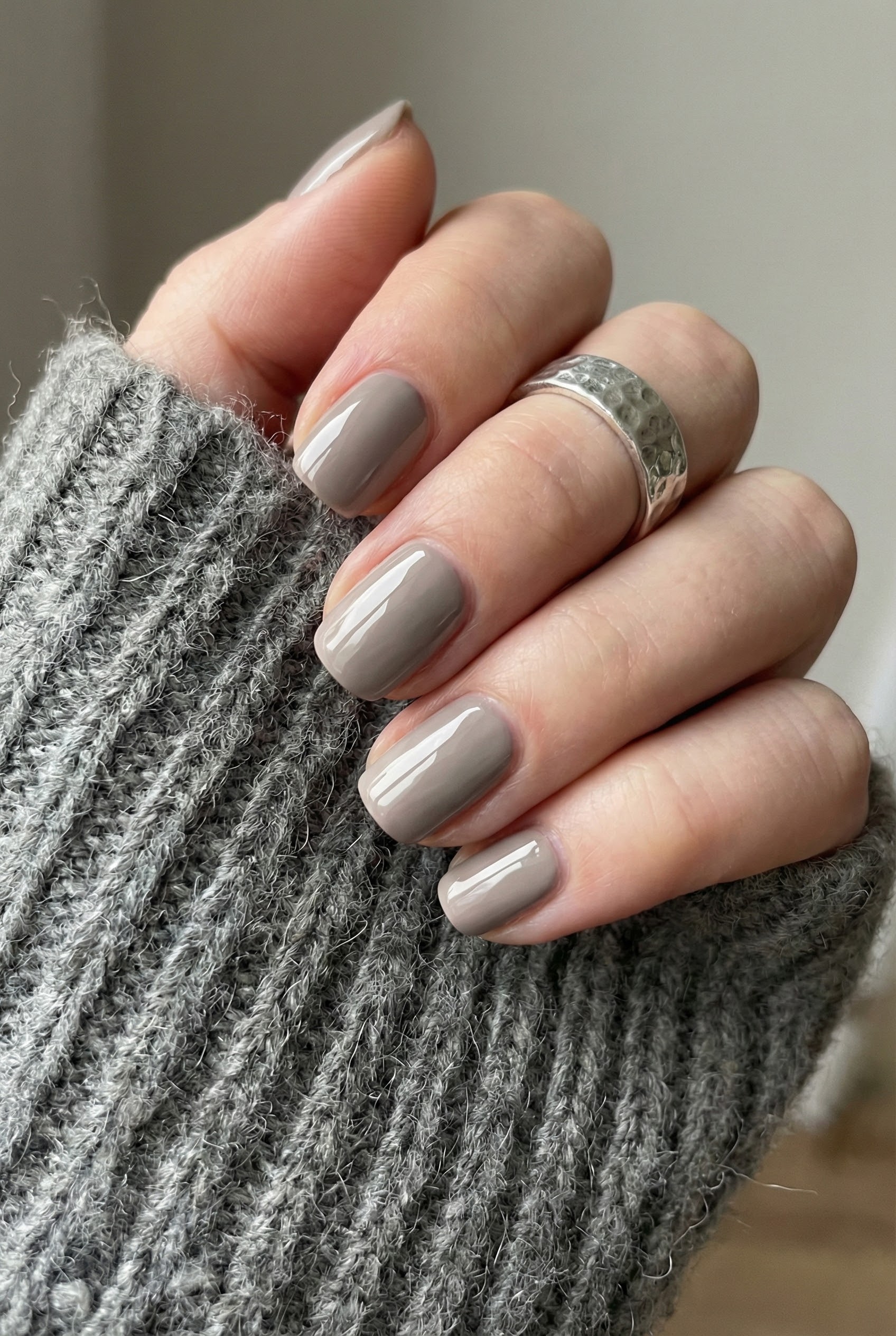 Glossy greige nails styled with a chunky grey knit sweater and a textured silver ring, showcasing a monochromatic look.