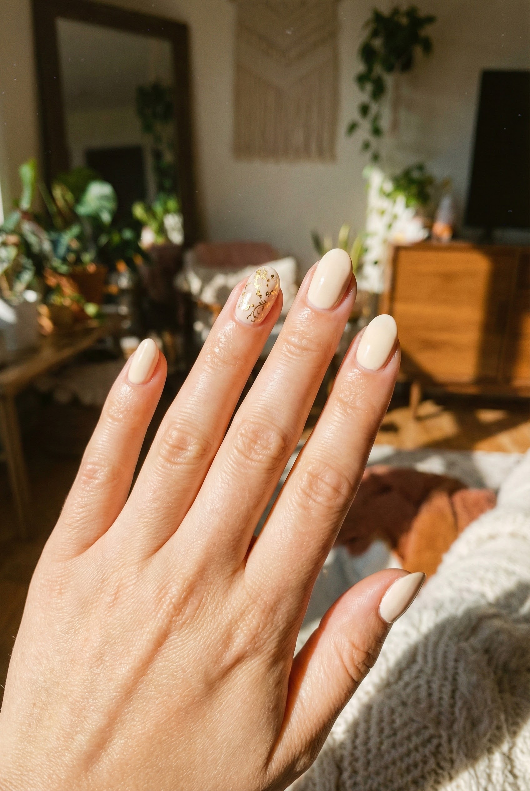The Rise of Soft Vanilla and Cream Nails 4 Lifestyle shot of vanilla nails with delicate gold foil nail art on the ring finger, captured in warm sunlight.