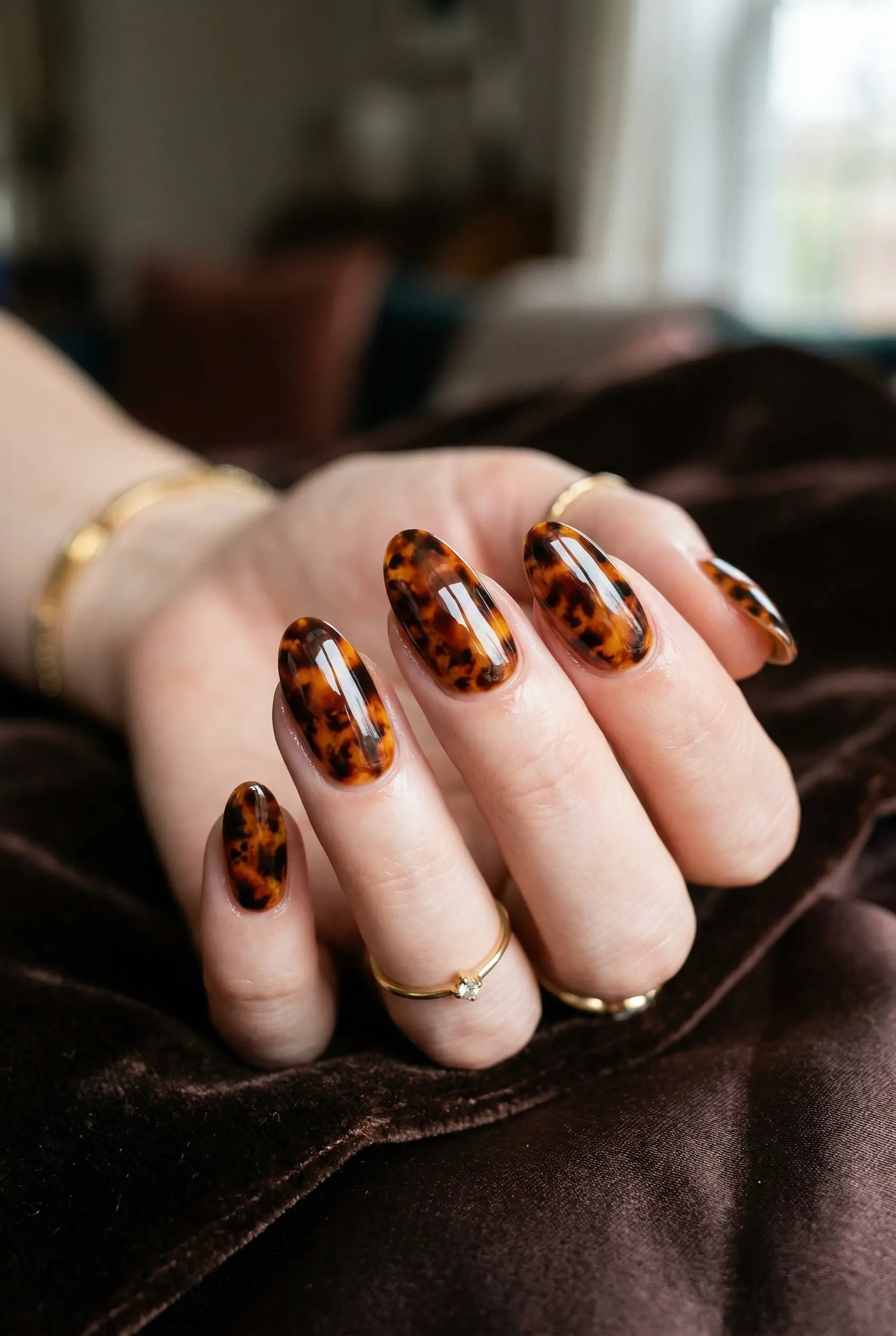 Glossy tortoiseshell pattern manicure on oval nails featuring rich amber, deep brown, and black tones layered like resin.