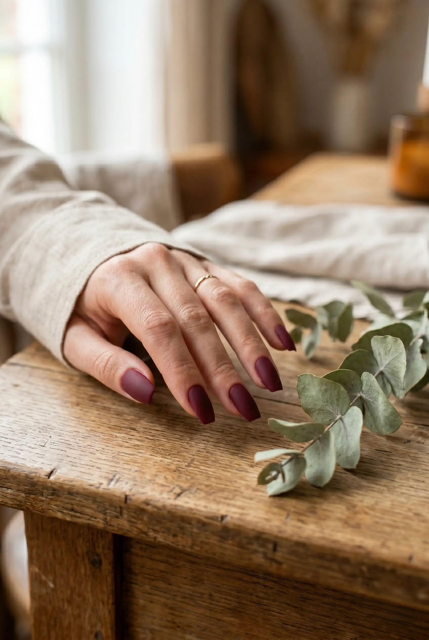 Close up of short coffin nails in a velvety matte burgundy finish on a rustic wooden table.