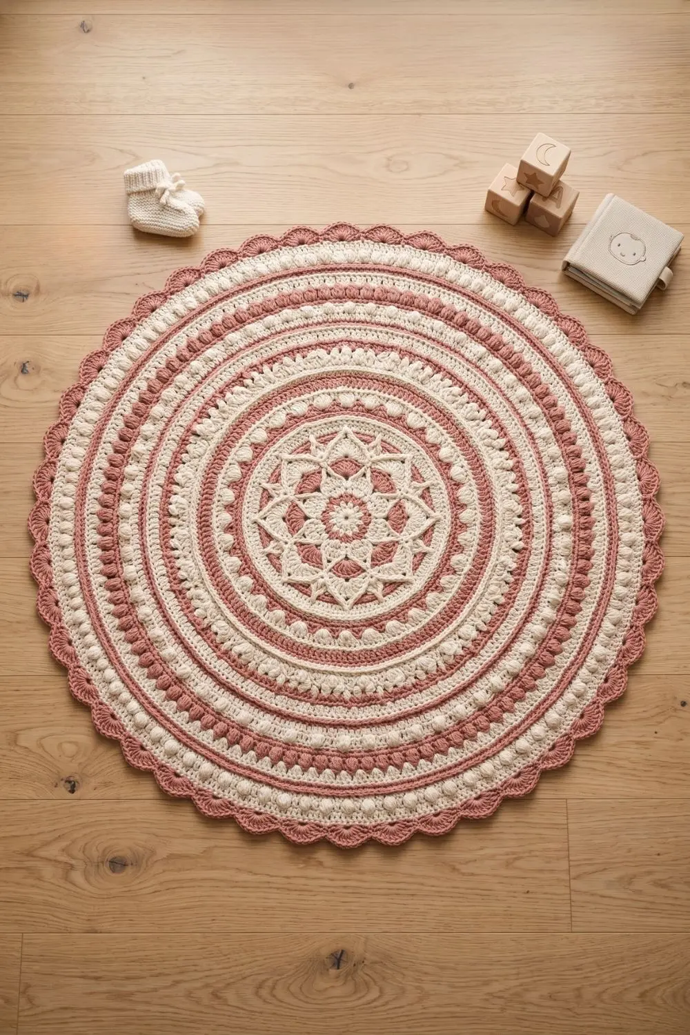 Round handmade crochet play mat in warm cream and dusty rose tones on a light oak nursery floor