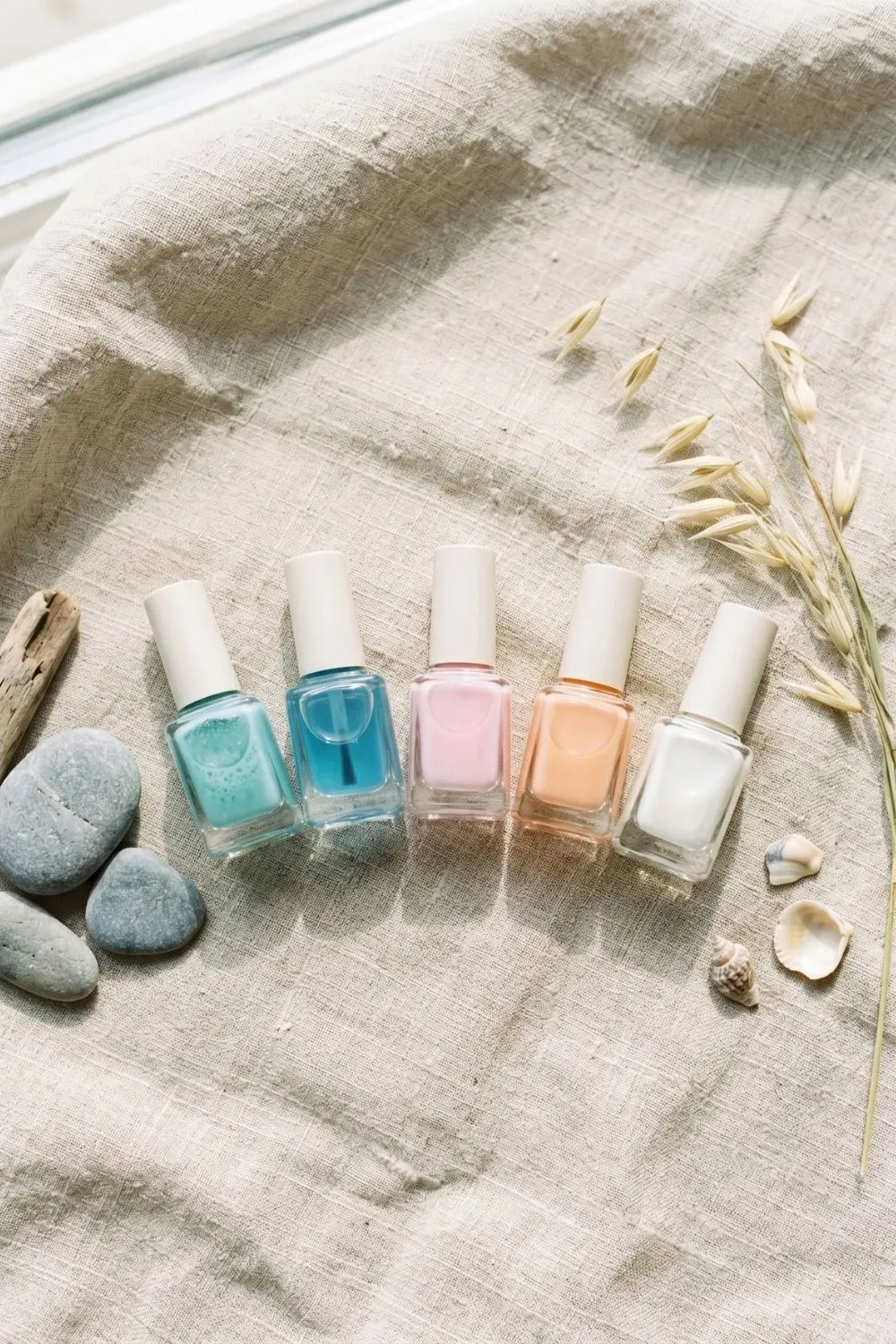 Sea-Glass Blue Jelly Nails: Summer 2026's Coastal-Calm Manicure 2 Flat lay of soft blue and milky nail polish bottles on linen with pebbles
