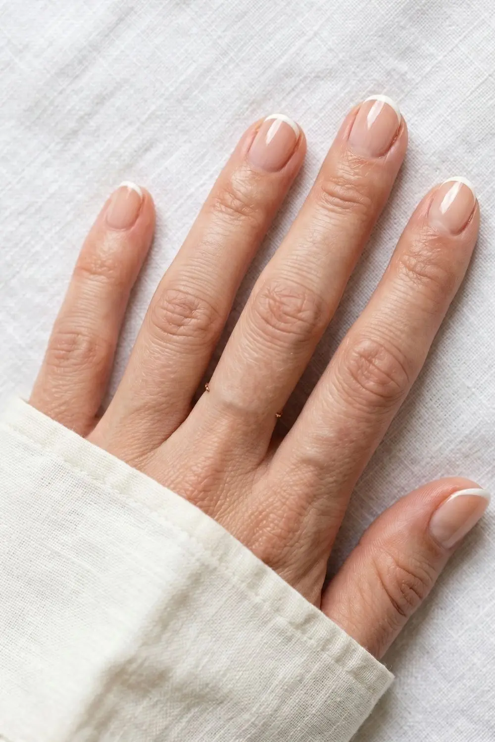 6 Modern French Tip Nail Variations Everyone Is Asking for Right Now 2 Close-up of short oval nails with an ultra-thin white micro French tip line on a neutral base