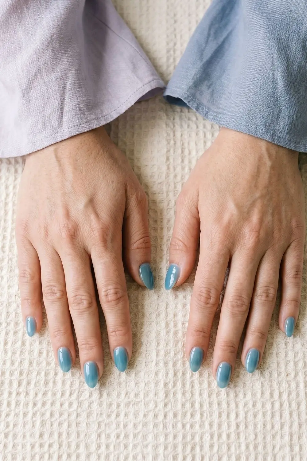Sea-Glass Blue Jelly Nails: Summer 2026's Coastal-Calm Manicure 3 Two hands with short almond nails in glossy sea-glass blue jelly polish on a towel