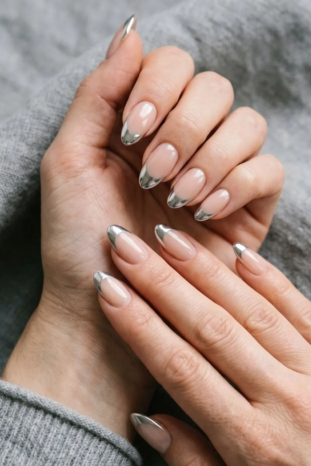 6 Modern French Tip Nail Variations Everyone Is Asking for Right Now 4 Close-up of almond nails with a chrome silver mirror-finish French tip on a nude base, grey sleeve at wrist