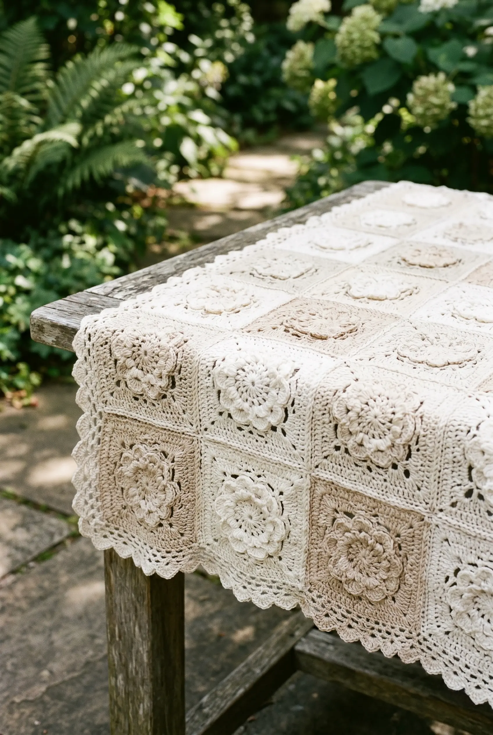 5 Vintage Aesthetics: Crochet Tablecloth Designs for Elegant Dining 4 Close-up vertical shot of a patchwork crochet tablecloth made from individual floral granny squares on a rustic outdoor garden table.