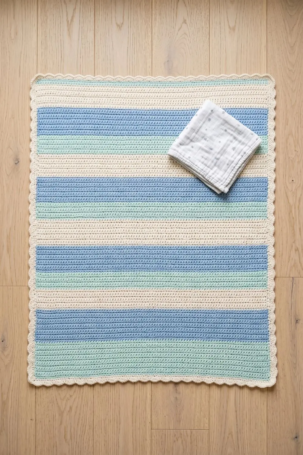 Rectangular crochet play mat with horizontal stripes in powder blue, cream and pale mint cotton on a light nursery floor