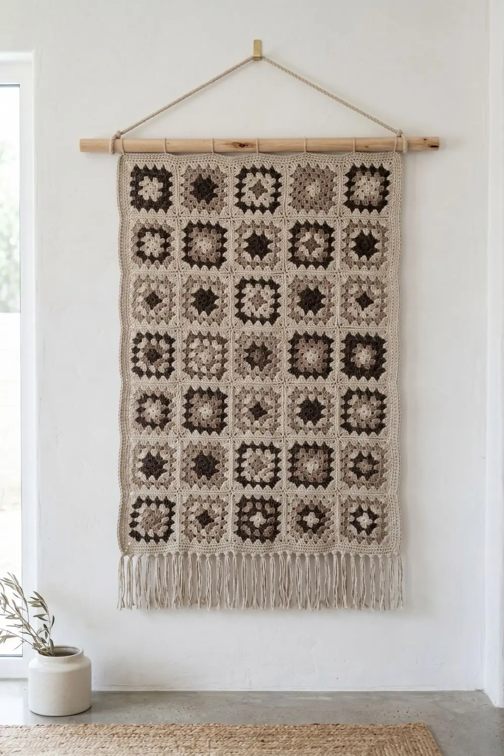 Granny Square, All Grown Up: Modular Crochet Designs Worth Showing Your Artisan 4 A large granny square wall panel in raw linen, soft taupe, and deep espresso tones, mounted on a wooden dowel against a white plaster wall. No people, even natural light.