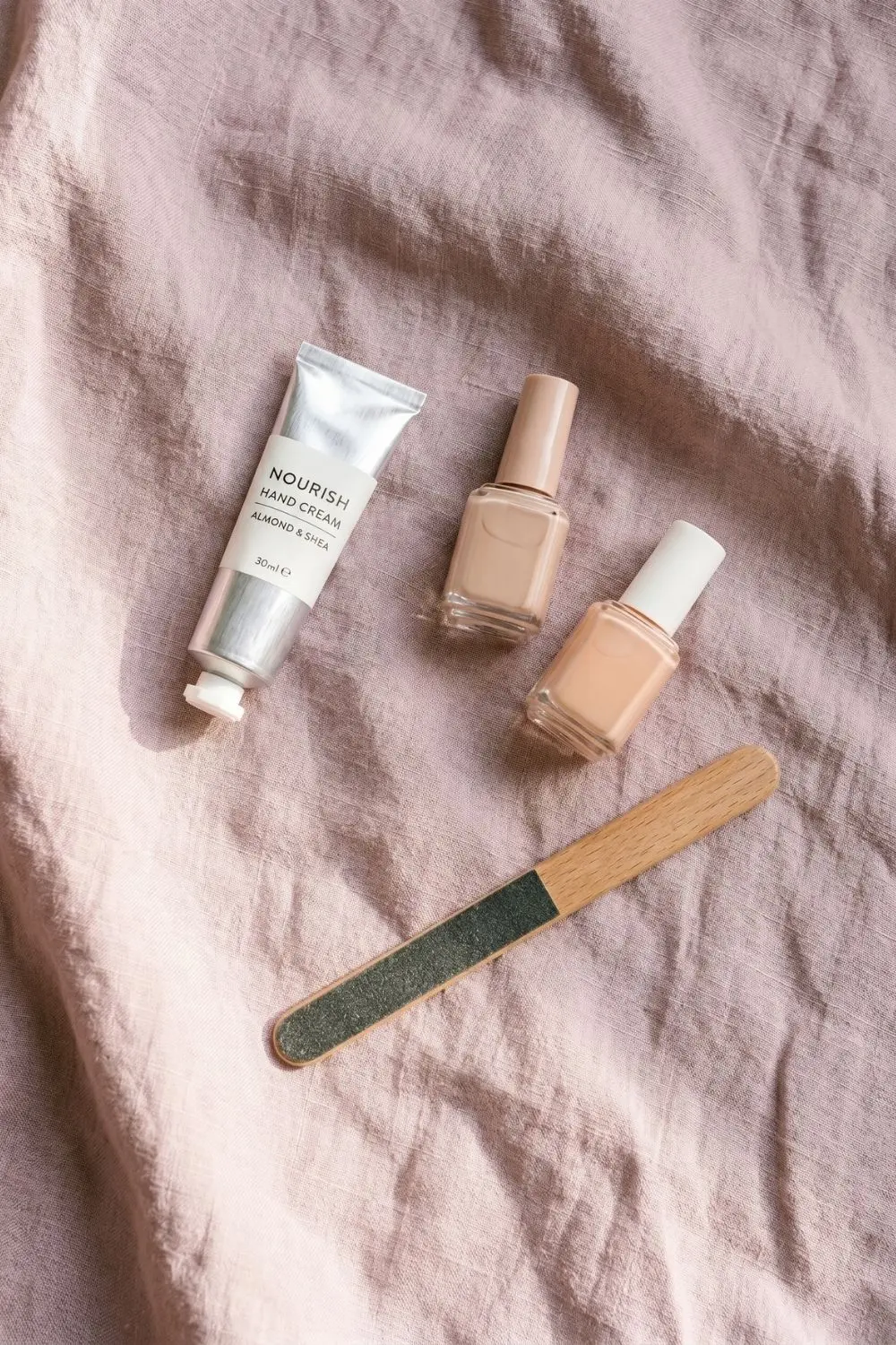 Why Women Are Filing Down Their Long Tips for This Nail Shape 5 Hand cream and nail polish bottles arranged on a soft linen background