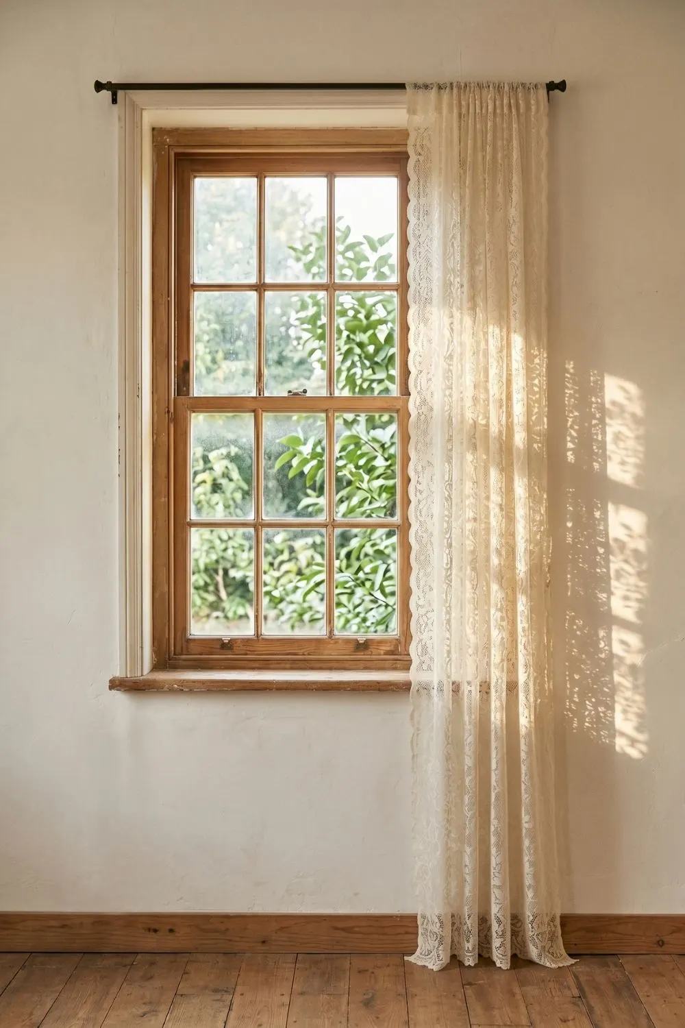 Sheer vintage lace curtain panel filtering light through its open-weave pattern at a tall window