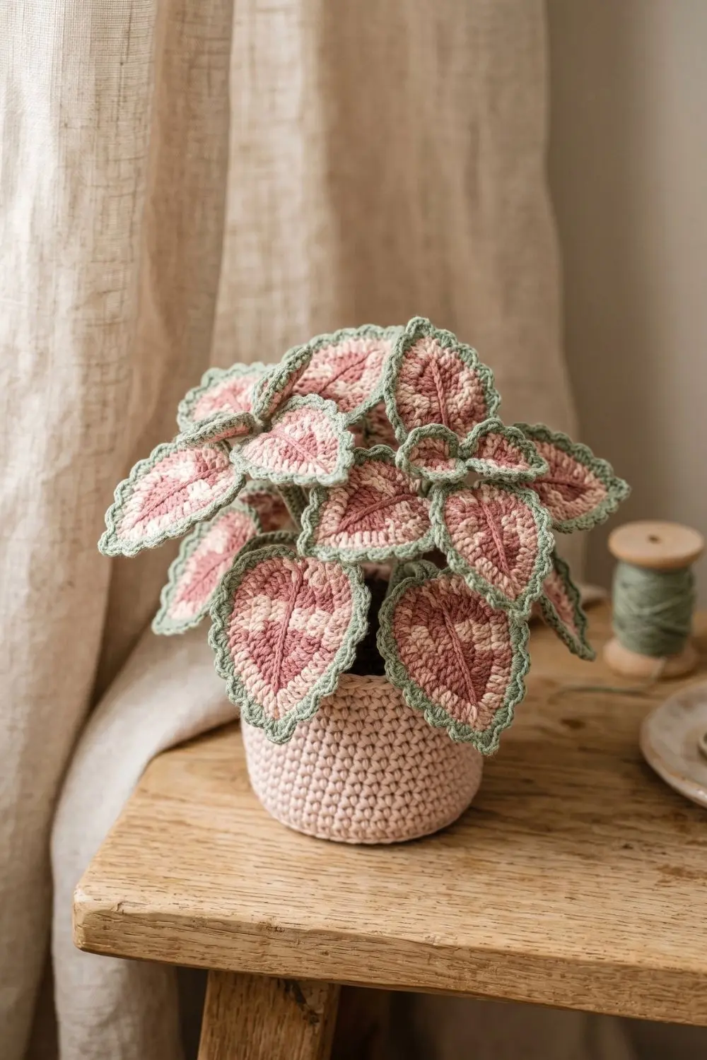 5 Crochet Plant Styles Dominating Pinterest Right Now 3 Crochet coleus plant in dusty rose and cream tones with sage-green scalloped edging in a pale blush pot on a rustic wooden surface
