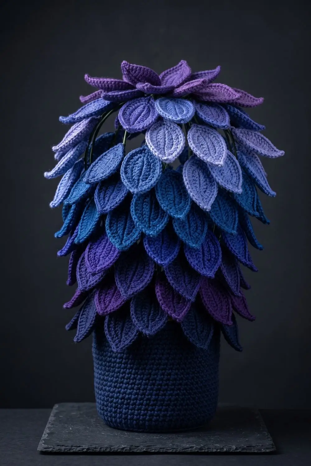 5 Crochet Plant Styles Dominating Pinterest Right Now 6 Crochet plant with cascading leaves in deep blue, violet and periwinkle tones in a dark navy pot against a charcoal background