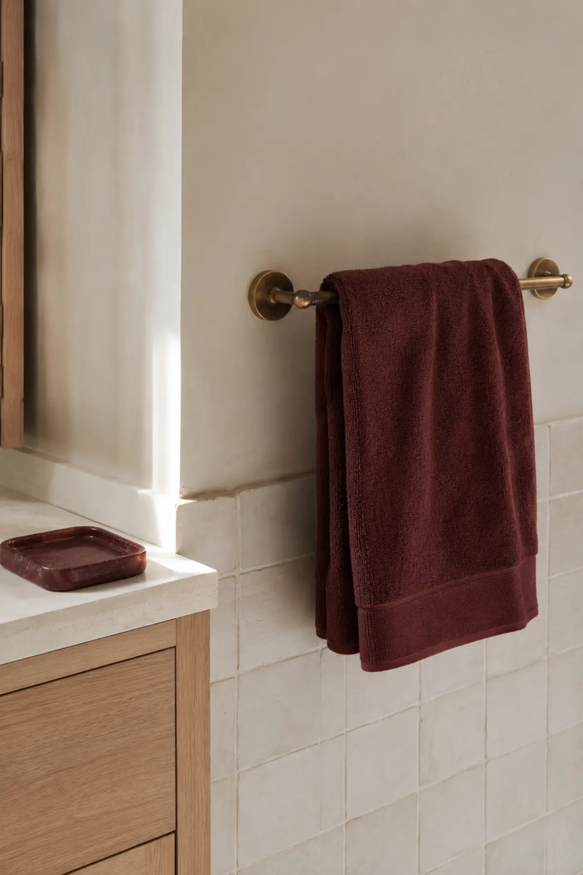 Muted oxblood towel and small stone tray adding removable color to a neutral bathroom